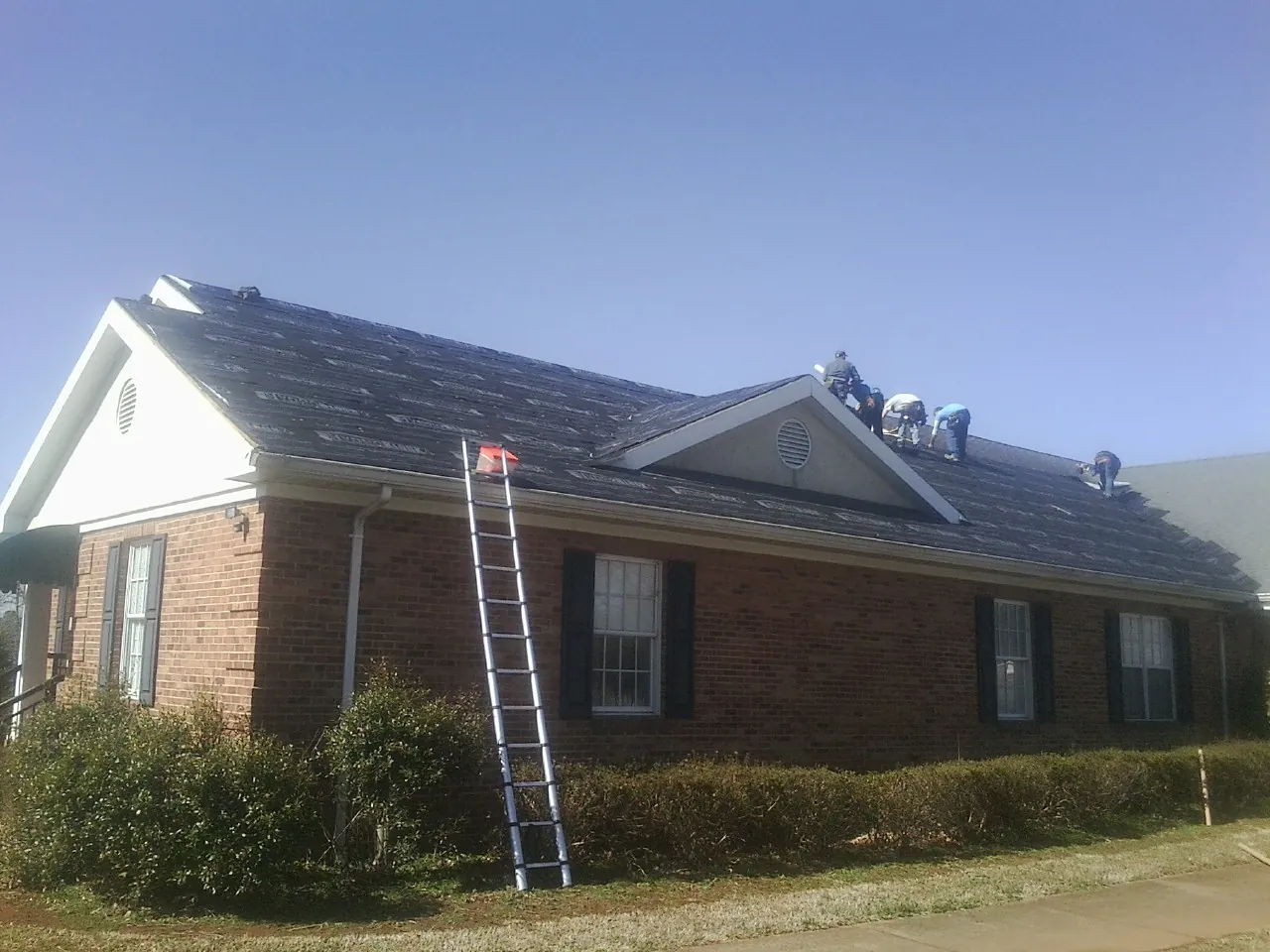 Crew tearing shingles off a brick ranch roof with a ladder set — Metal Roof Repair work by our crew in Parlin