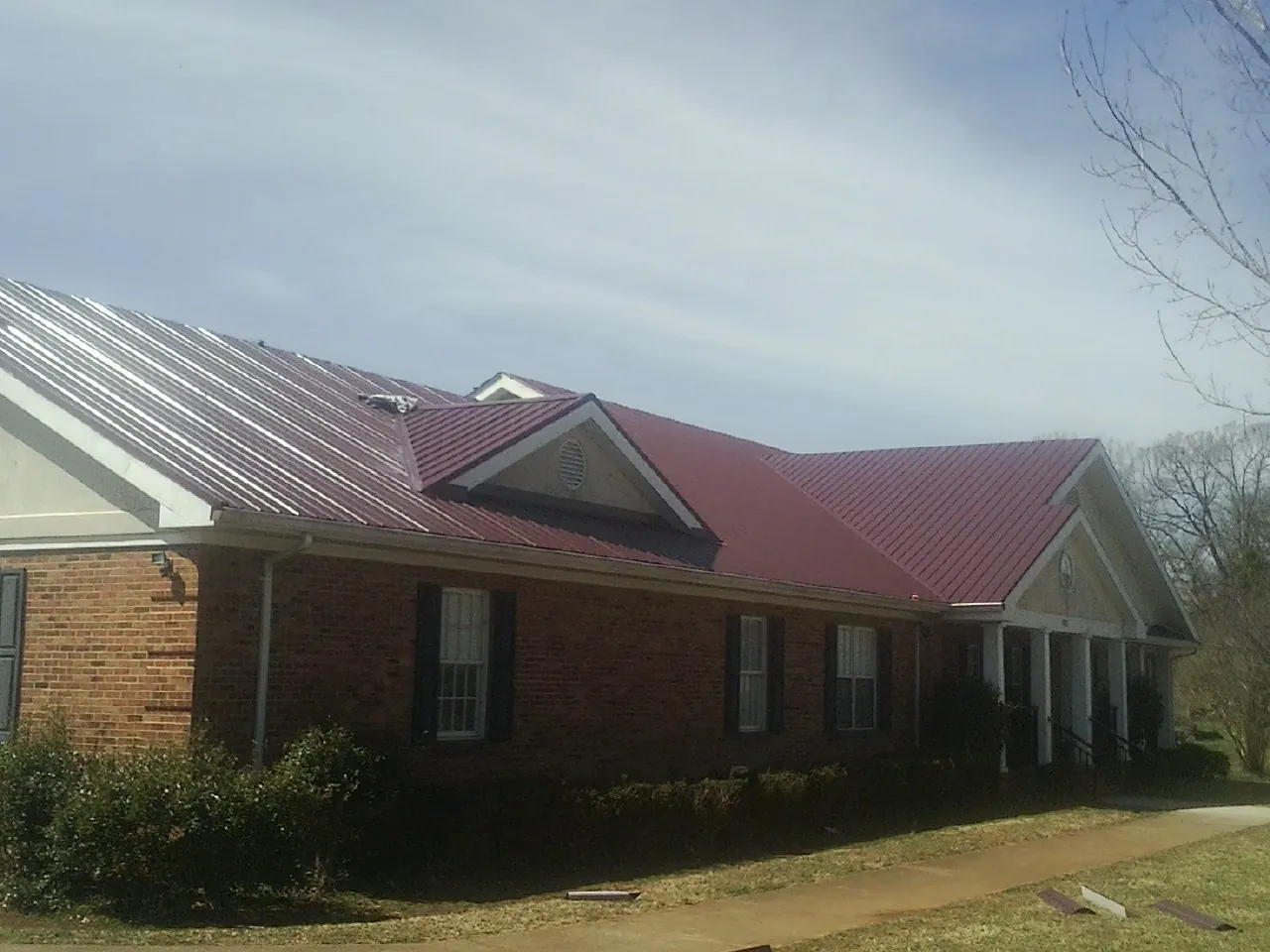 Red metal roof with gabled entries on a long brick building, from a Hail Damage Roof Repair job in Parlin